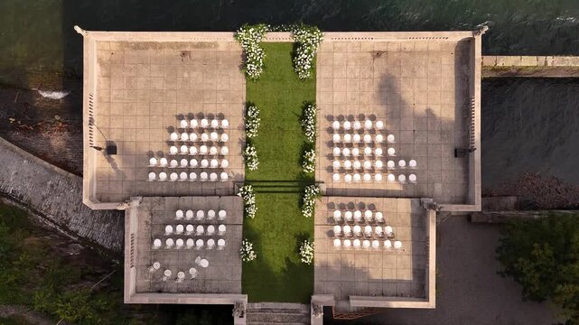 Drone aerial view of Villa Pizzo terrace on Lake Como decorated for luxury wedding ceremony with floral arch and elegant rows of chairs overlooking the scenic water and mountains