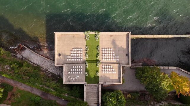 Drone aerial view of Villa Pizzo terrace on Lake Como decorated for luxury wedding ceremony with floral arch and elegant rows of chairs overlooking the scenic water and mountains