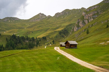 Scenic mountain landscape featuring rustic wooden cabin surrounded by lush green hills and winding...