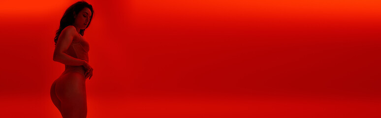 Young woman poses confidently against vibrant red backdrop in a striking artistic setting