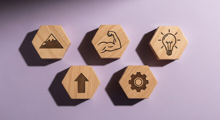 Fototapeta premium Five wooden hexagonal tiles with icons representing mountain, bicep, lightbulb, upward arrow, and gear, arranged in a scattered pattern on a purple background