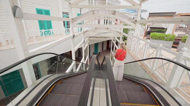 Young woman going down a moving escalator in an open air colorfull commercial center, puerto colombia, barranquilla