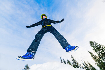 Boy enjoys playful winter moments while jumping in the snow in Sweden surrounded by trees and blue sky