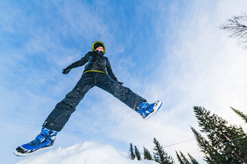 Boy enjoys playful winter moments while jumping in the snow in Sweden surrounded by trees and blue sky