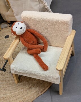 Mu&ntilde;eco de simio de peluche sentado en sill&oacute;n con alfombra en habitaci&oacute;n infantil 