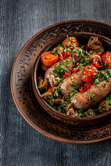 Baked sausages with vegetables and herbs in clay bowl