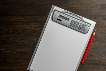 Clipboard with a white blank paper and red pencil on wooden table, closeup, top view. Grey desktop...
