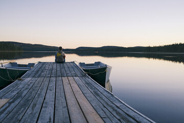 Québec, Canada. Une femme seule se détend au bout du quai. Lever de soleil sur le lac en forêt.