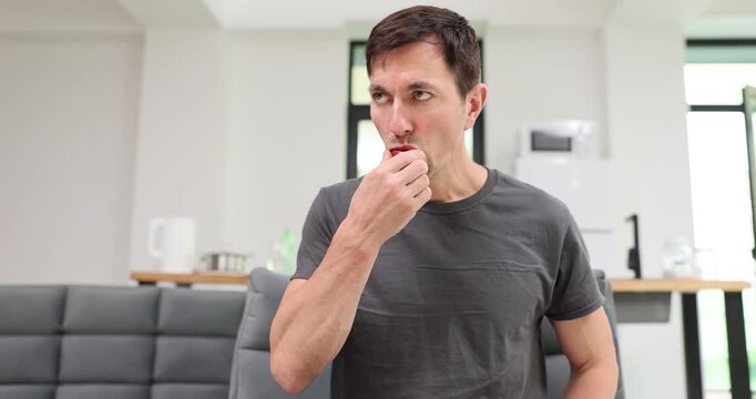 Man holds tomato and takes small bite tasting juice sitting at sofa. Taster chews piece with lips evaluating flavor of fresh snack slow motion