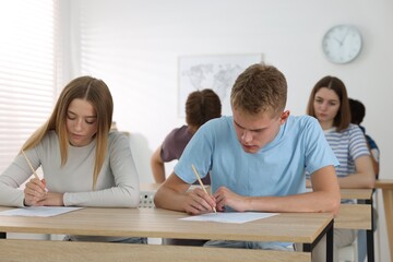 Fototapeta premium Students taking exam at wooden table indoors