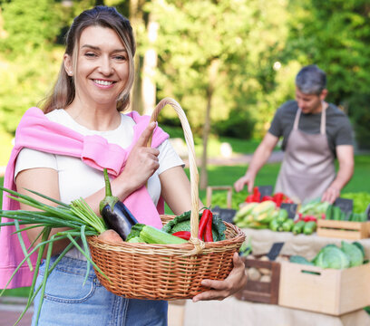 Woman with different fresh vegetables in wicker basket at farmer's market, selective focus