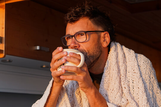 Digital nomad traveling in his camper van. Drinking a hot beverage while watching the sunset.