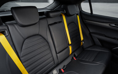 Rear leather seats with yellow seat belts in a car. Hatchback or SUV interior with black leather...
