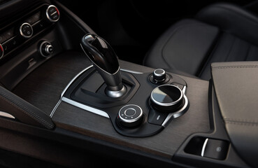 Automatic gear selector and driving mode knobs in luxury car. Automobile interior in dark tones, close-up view of bottom part of center console with automatic gear selector and driving controls.