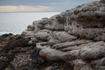 Rugged volcanic rock formations meet the serene ocean under a cloudy sky, showcasing natural...