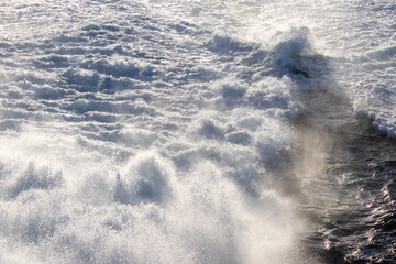 Dynamic ocean waves generating abundant white foam and fine mist under bright natural light.