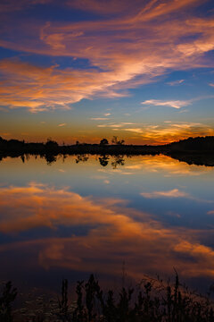 Brilliant sunset sky with vivid orange and pink clouds mirrored in the still waters of a Pine Barrens lake during a calm and peaceful evening.