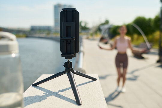 Smartphone on tripod recording Young woman skipping rope outdoors near river fitness enthusiast exercising while camera capturing workout session