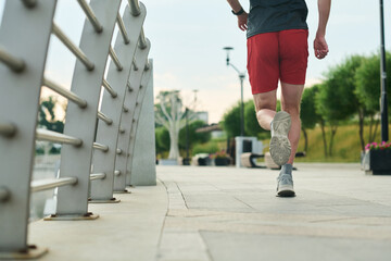 Young man jogging along urban riverside path athletic build visible from behind wearing running shoes exercising outdoors on paved walkway near metal railing