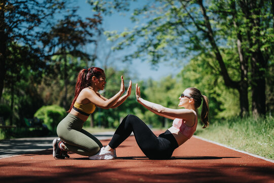 Two active women engaging in outdoor fitness, practicing partner exercises on a sunny trail surrounded by nature.