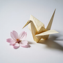 Delicate paper origami crane next to soft pink blossom on clean white background