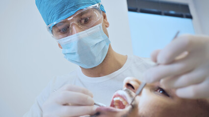 A focused dentist in surgical attire examines a patient's mouth, highlighting precision and care in dental health. The clinical setting underscores professionalism, emphasizing the importance.