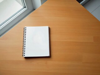 Blank notebook on a wooden table by the window with ample copy space for design