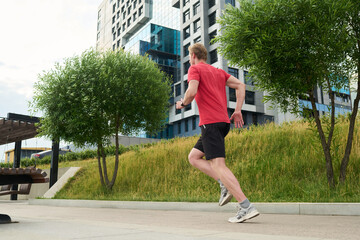 Young man jogging outdoors near modern apartment buildings running on paved path surrounded by green grass and trees athletic activity in urban environment