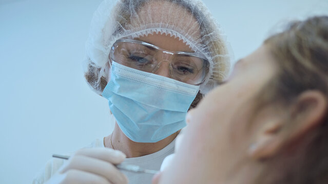 A dentist in protective gear examines a patient's mouth, emphasizing dental health and meticulous care. The clinical setting highlights professionalism and attention to detail in healthcare.