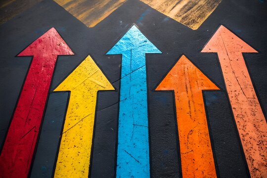 Multiple colorful arrows are painted on a dark background, all pointing upwards, symbolizing progress, growth, and forward movement in various directions on a textured surface.