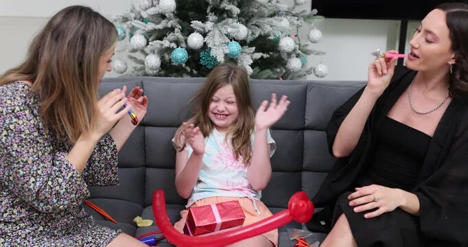 Happy women with little girl celebrate Christmas with gift air balloons and party horns at home. Daughter with mother and aunt on Xmas holiday