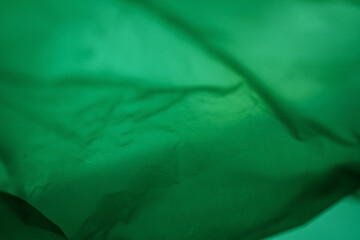 Extreme close up of green empty plastic bag background. The plastic surface is wrinkly and tattered making abstract pattern. Selective focus, shallow depth of field.