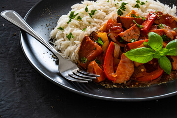 Polish lecho with white rice - bell pepper tomato stew with sausages on black table