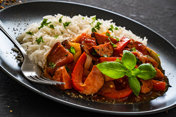 Polish lecho with white rice - bell pepper tomato stew with sausages on black table