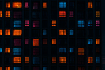 Abstract pattern of illuminated building windows at night creating a geometric grid of glowing squares in warm and cool tones against a dark background
