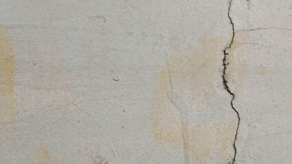 An old concrete wall showing cracks and weathered texture, its surface showing fine brown stains, rough edges and natural imperfections.