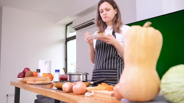 Young woman chef in apron enjoys slice of freshly baked pumpkin pie with delighted smile. Housewife enjoys taste of homemade pumpkin pie in kitchen