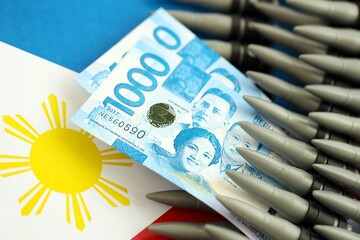 Philippines peso currency money bills and rifle bullets on flag. The concept of warfare and gun...
