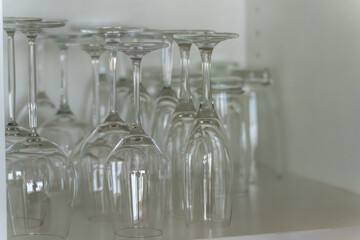 Several empty wine glasses stand upside down in a cabinet. The clear glass reflects the light.
