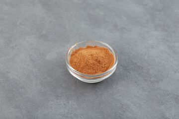 Natural Guarana seed powder in glass bowl on grey background. Cupana tea extract rich in caffeine. Guarana used in sweetened or carbonated soft drinks and energy drinks
