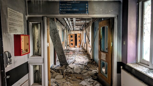 Derelict abandoned hospital hallway entrance, collapsing corridor doorway debris. Eerie deserted vandalised NHS medical facility falling apart in disrepair. Natural disaster earthquake aftermath.