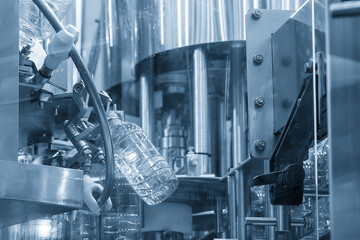 The  empty drinking water bottles  hanging on the overhead conveyor belt for filling process in the light blue scene