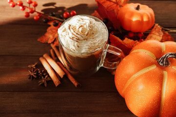 Warm pumpkin spice drink with whipped cream and autumn decor on wooden table