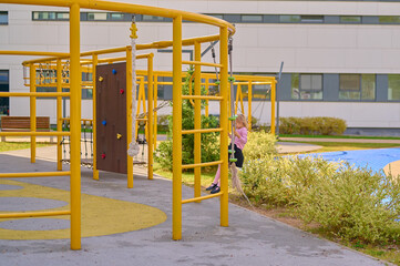 Child climbing yellow playground structure in urban park