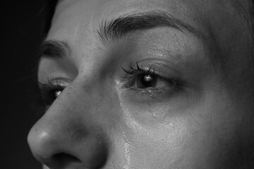 Sad woman crying on dark background, closeup. Black and white effect