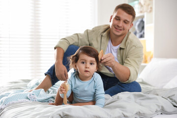 Fototapeta premium Father combing his baby's hair on bed at home