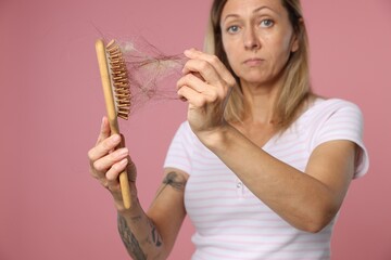Alopecia problem. Worried woman taking her lost hair from brush on pink background