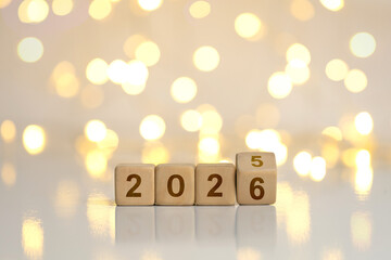 Wooden cube blocks flipping from 2025 to 2026 on warm golden bokeh, symbolizing New Year goals, resolutions, countdown and fresh start, with copy space for holiday promotions and seasonal greetings.