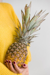 A girl in a bright yellow sweater holds fresh juicy pineapple in her hands
