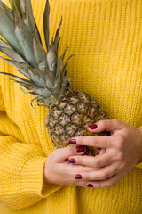 A girl in a bright yellow sweater holds fresh juicy pineapple in her hands